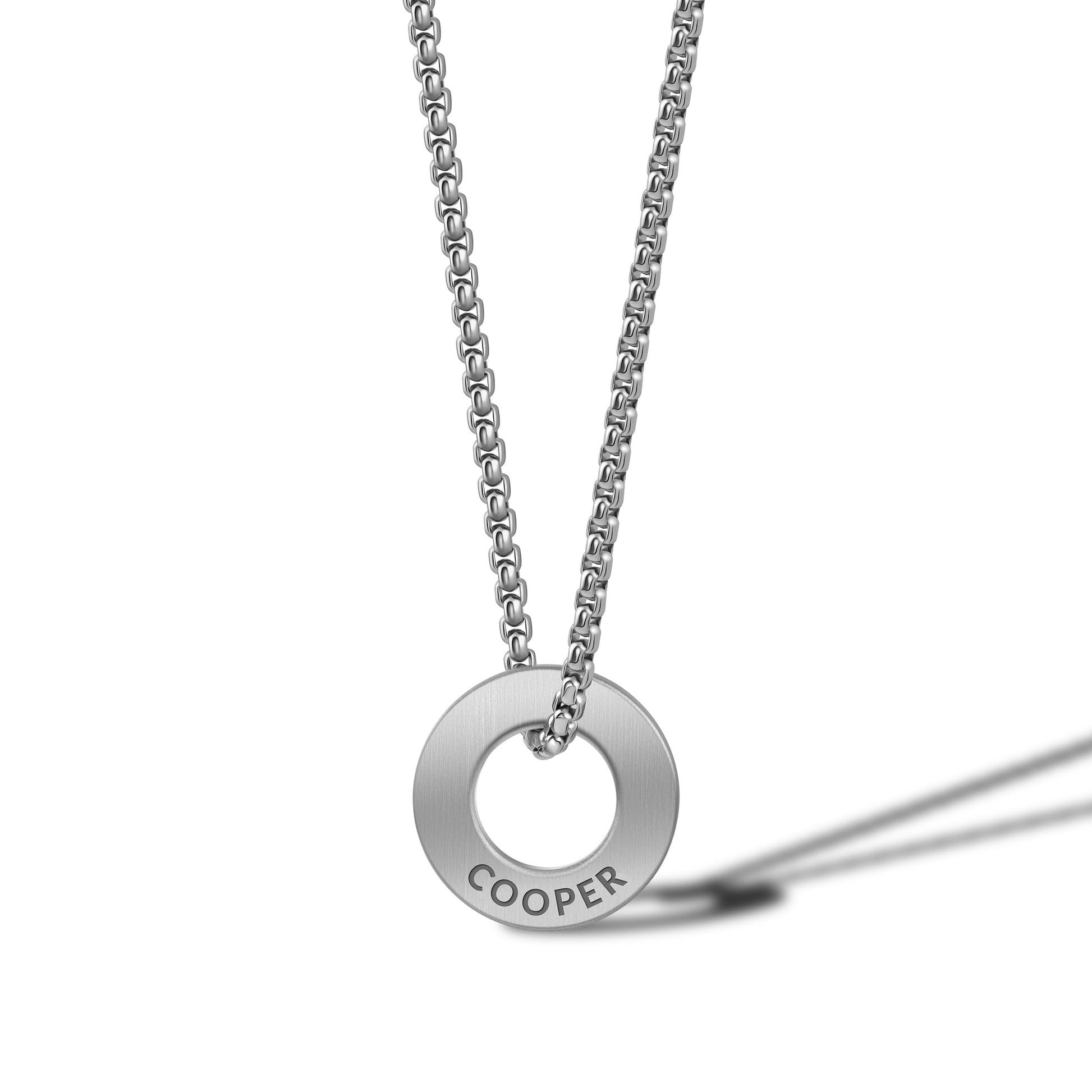 Silver necklace with a round pendant engraved with 'COOPER' on a white background