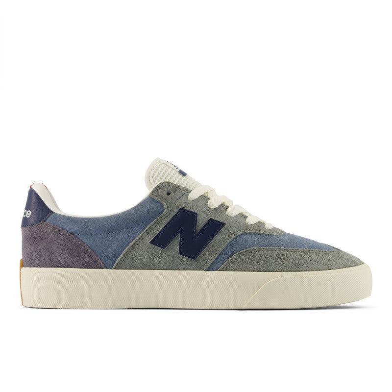 A New Balance sneaker in a muted colorway featuring dusty blue suede, gray suede, a dark navy 'N' logo, and an off-white rubber sole and laces, shown from a side profile on a white background.